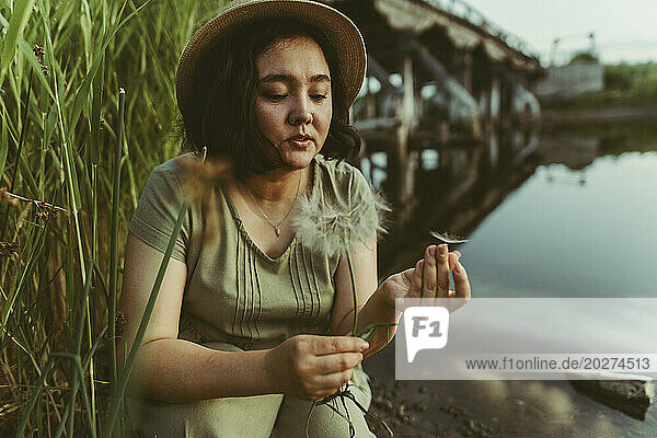 Woman holding dandelion seeds near lake