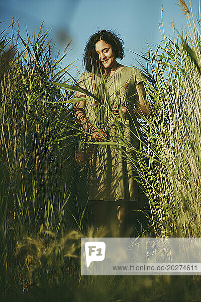 Smiling mature woman standing amidst tall grass in field
