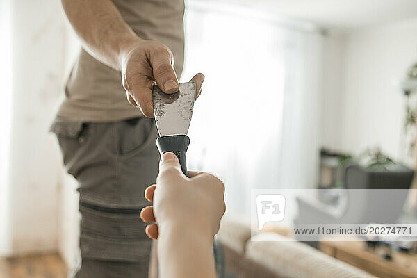 Son passing spatula to father renovating home