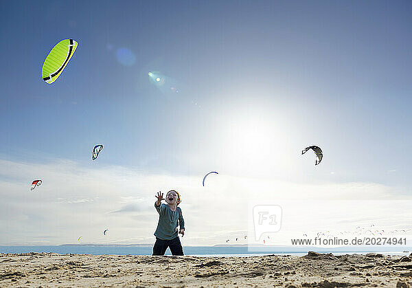 Cheerful boy watching kite surfers at beach on sunny day