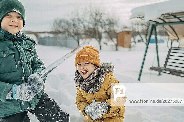 Cheerful siblings playing with icicle in snow