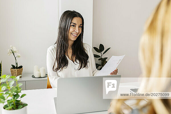 Happy HR manager holding resume and discussing with candidate in office