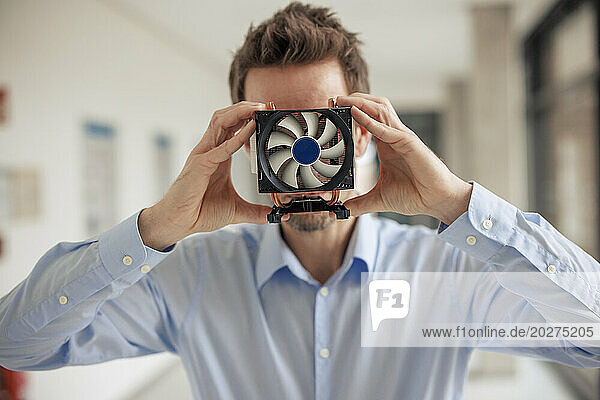 Mature engineer covering face with CPU fan at workshop