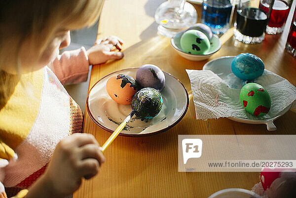 Girl painting on Easter eggs in plate at home