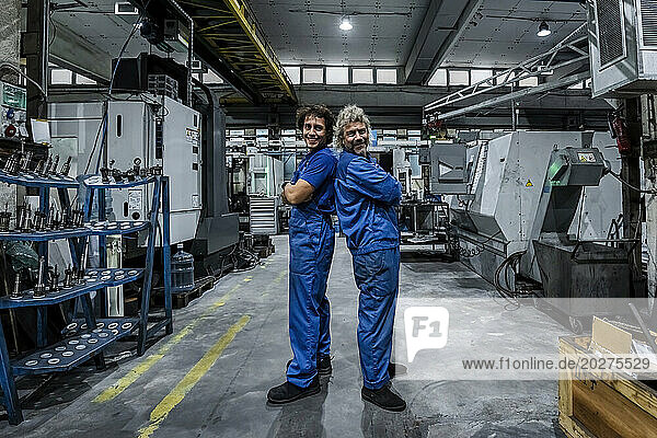 Smiling technicians standing back to back with arms crossed in industry