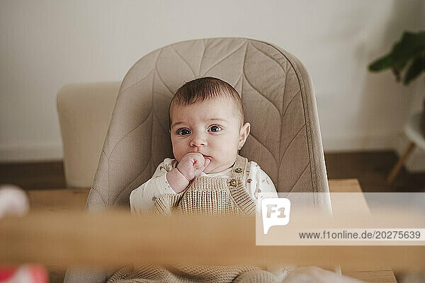 Baby girl sitting with hand on mouth on bouncer chair