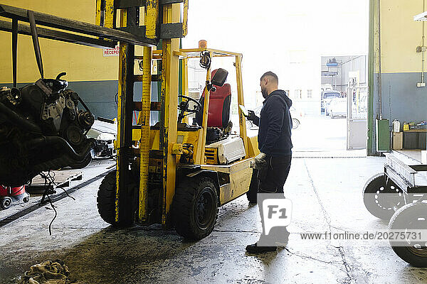 Mechanic using smart phone near forklift at workshop