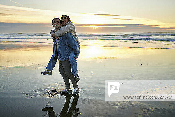 Smiling man carrying girlfriend piggyback at ocean beach