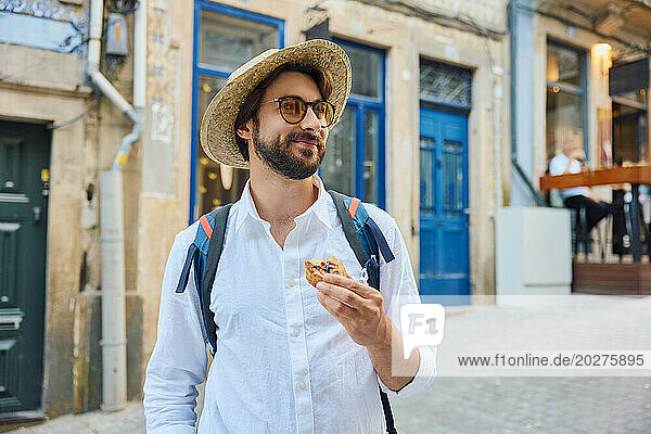 Man holding traditional dessert pastel de nata and standing in front of building