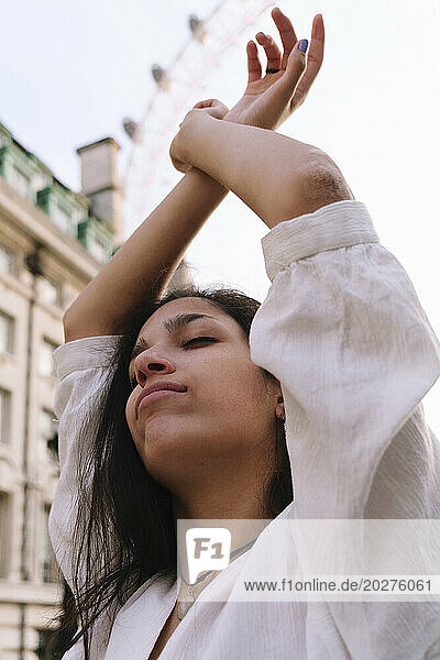 Young woman with arms raised and eyes closed in city