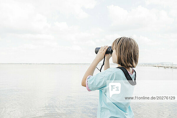Girl looking at lake through binoculars