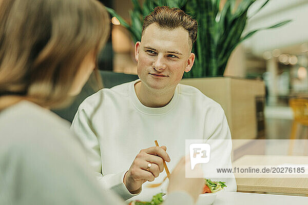 Young man eating salad with girlfriend at mall