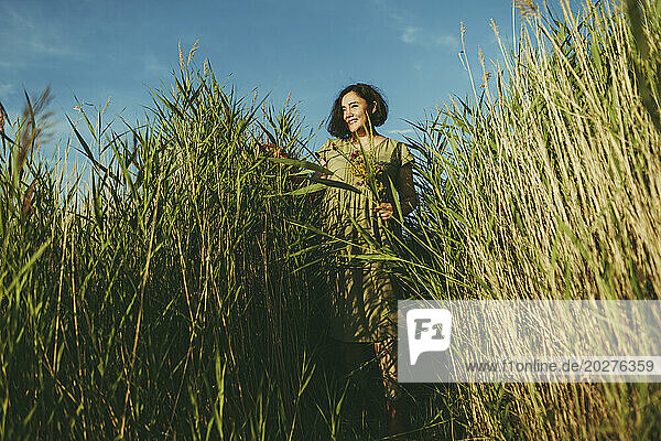 Carefree mature woman standing amidst tall grass in field