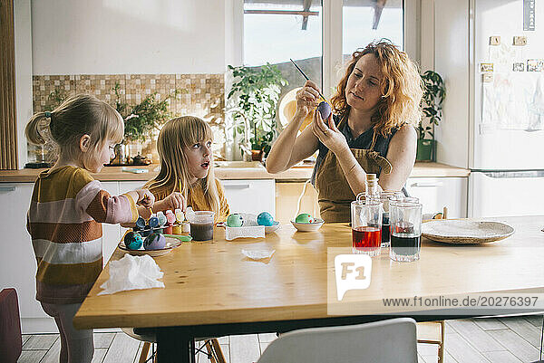 Woman coloring Easter egg with daughter sitting at home