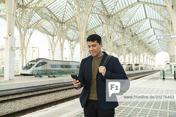 Smiling businessman using smart phone at station platform