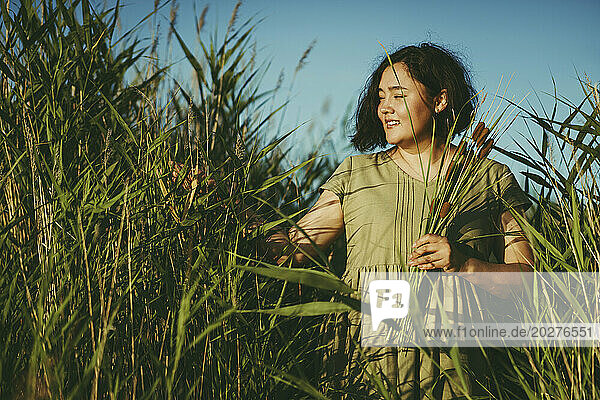 Smiling mature woman touching grass in field