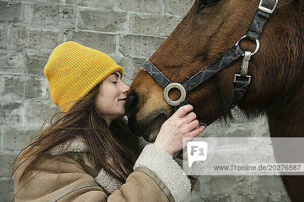 Woman kissing bay horse in front of wall