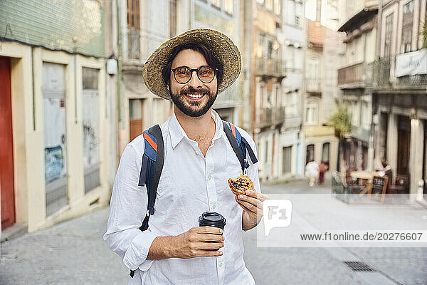Smiling young man holding coffee cup and traditional dessert pastel de nata