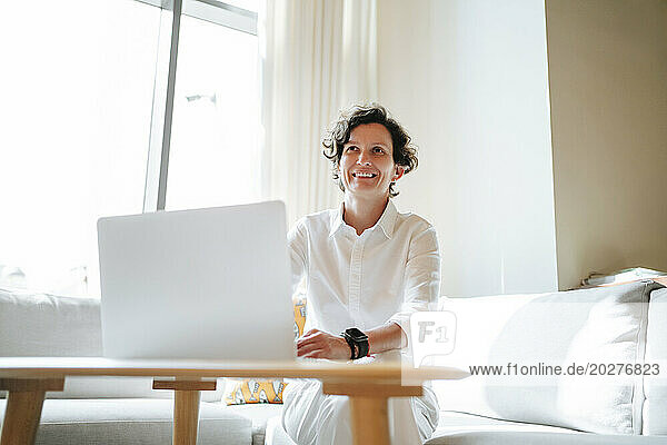 Smiling mature businesswoman with laptop sitting on sofa in lobby of hotel