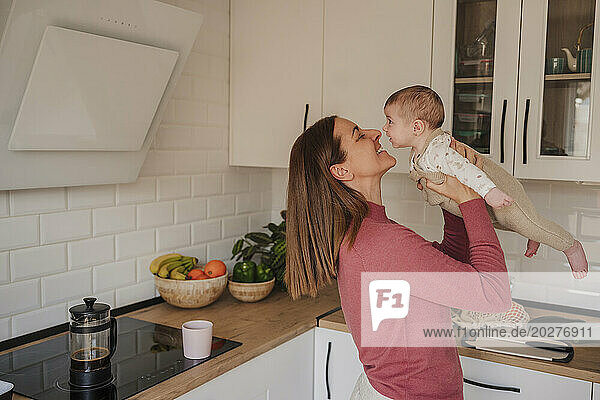 Smiling mother embracing and playing with baby daughter in kitchen