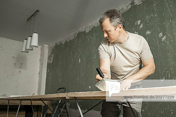 Man applying glue on new wallpaper at workbench in living room