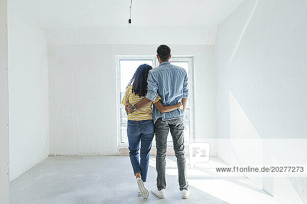Young couple standing with arms around at new home
