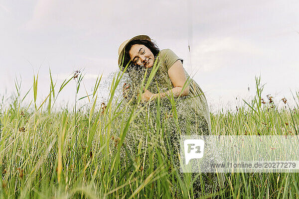 Smiling woman embracing gypsophila flowers amidst grass in field