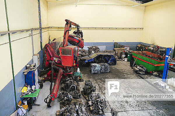 Mechanic operating crane machine to carry scrap vehicles at workshop