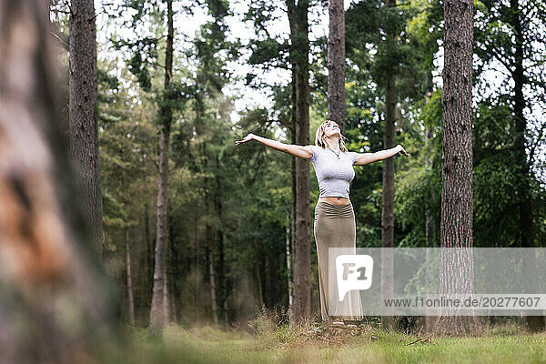 Young woman standing with arms outstretched in front of trees at forest