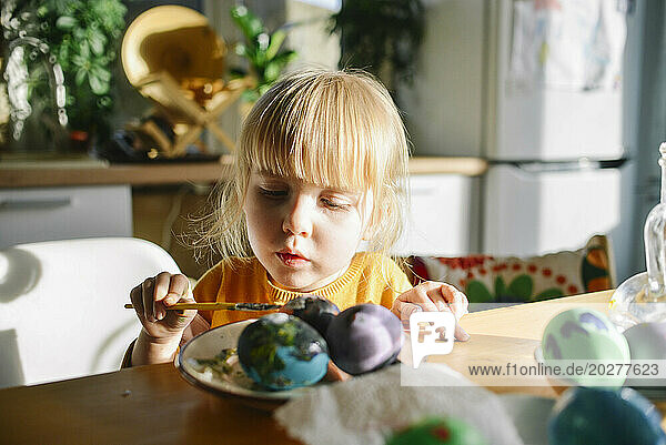 Girl with bangs coloring Easter eggs at home