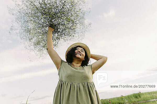 Playful mature woman carrying bunch of gypsophila above head in field