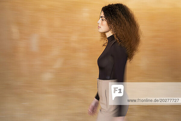 Young woman walking against brown background
