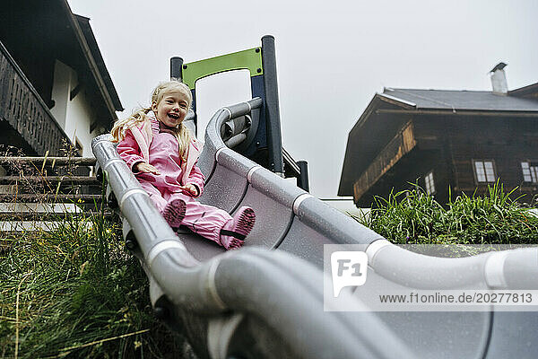 Girl in pink raincoat sliding down slide at playground
