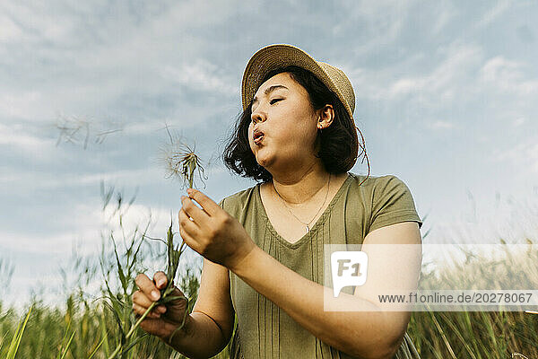 Carefree mature woman blowing on dandelion in field