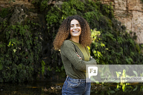 Happy young woman standing with arms crossed at park