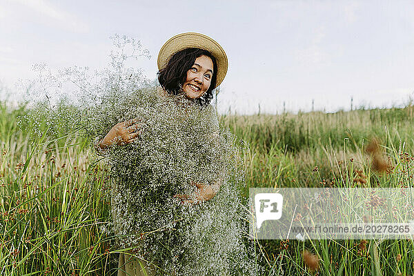 Happy mature woman holding bunch of gypsophila flowers in field