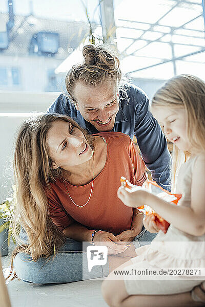 Happy mother and father with girl holding snacks at home