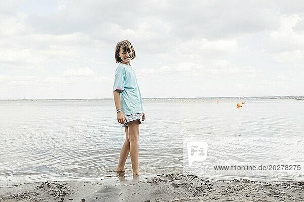 Happy girl standing near shore by lake
