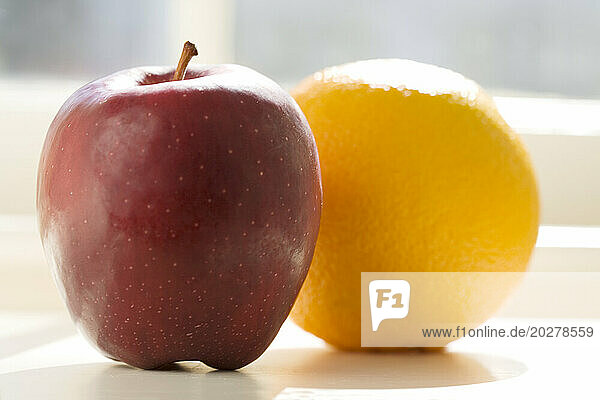 Apple and orange on table in sunlight