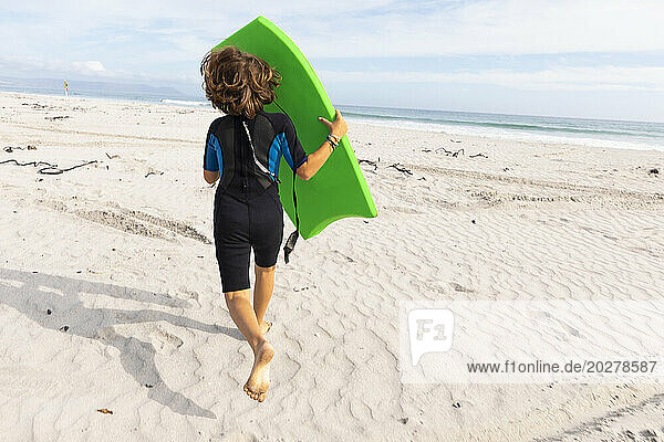 South Africa  Hermanus  Rear view of boy running on beach with body board