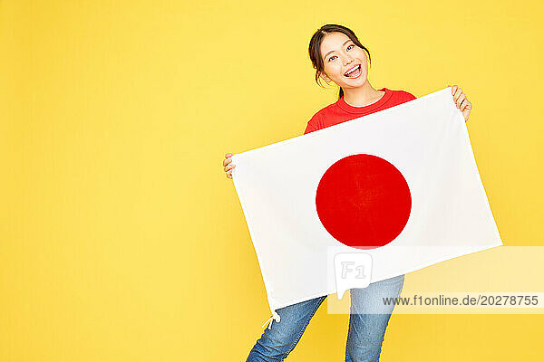 Eine Frau hält eine japanische Flagge auf gelbem Hintergrund