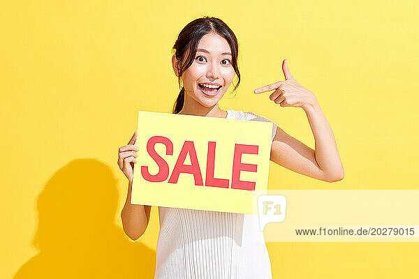 Asian woman holding up a sale sign on yellow background