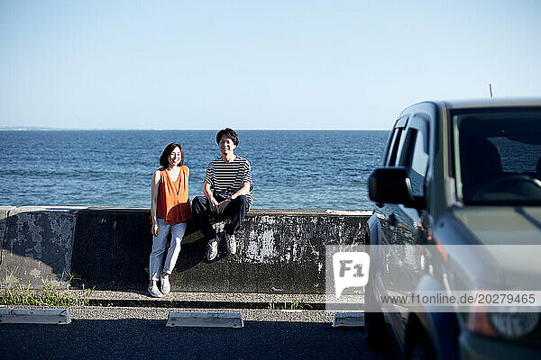 A couple sitting on a wall near the ocean