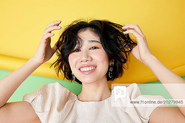 A woman with short hair smiling and holding her hair
