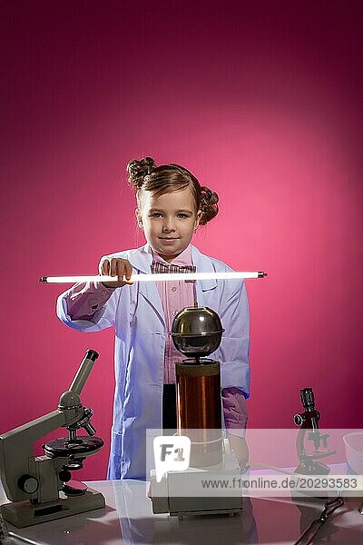 Ernsthafte kleine Physikerin zeigt Fokus mit Lampe  auf rosa Hintergrund