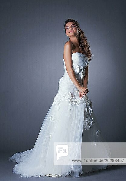 Verträumte Brünette posiert in elegantem Hochzeitskleid  auf grauem Hintergrund
