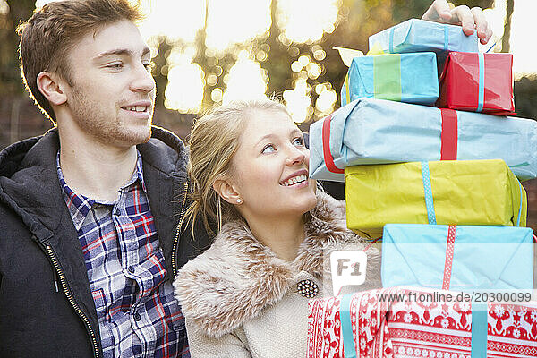 Young Couple Holding Stack of Christmas Presents Outdoors