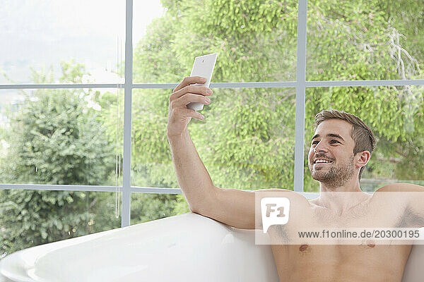 Smiling Man in Bathtub Taking Selfie