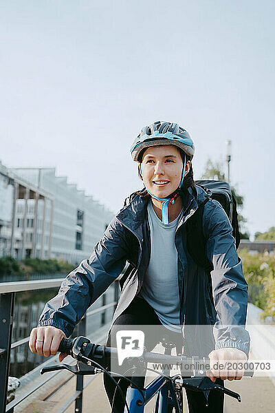 Smiling female delivery person wearing helmet and sitting on bicycle