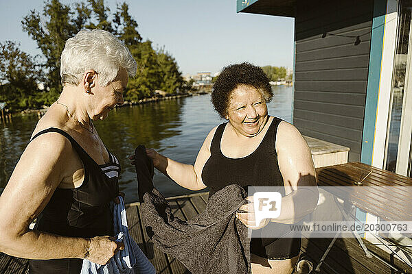 Happy senior female friends holding towel while standing on houseboat at sunny day